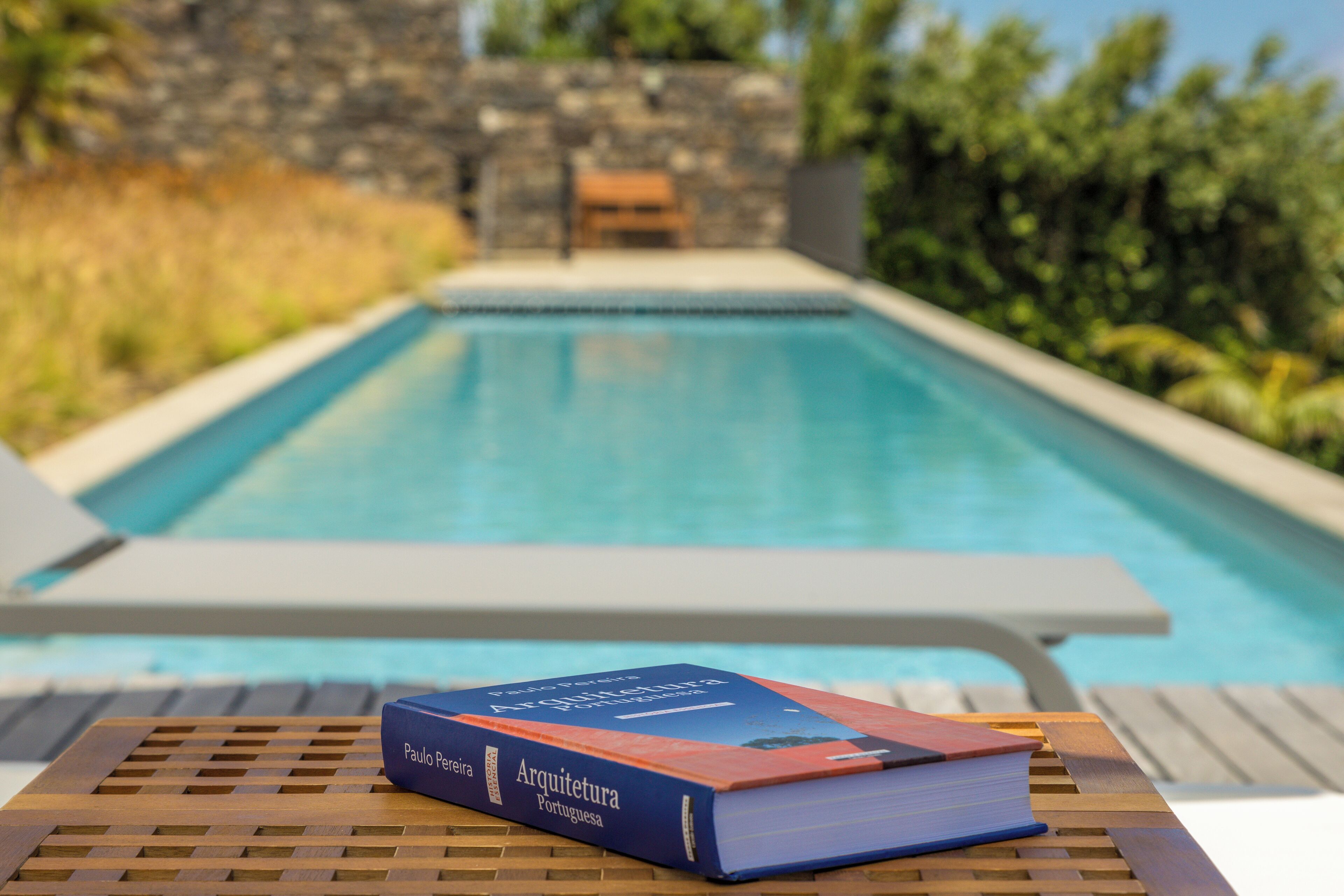 Ein Poolbereich mit Liegestuhl und einem Tisch, auf dem das Buch "Arquitetura Portuguesa" liegt.