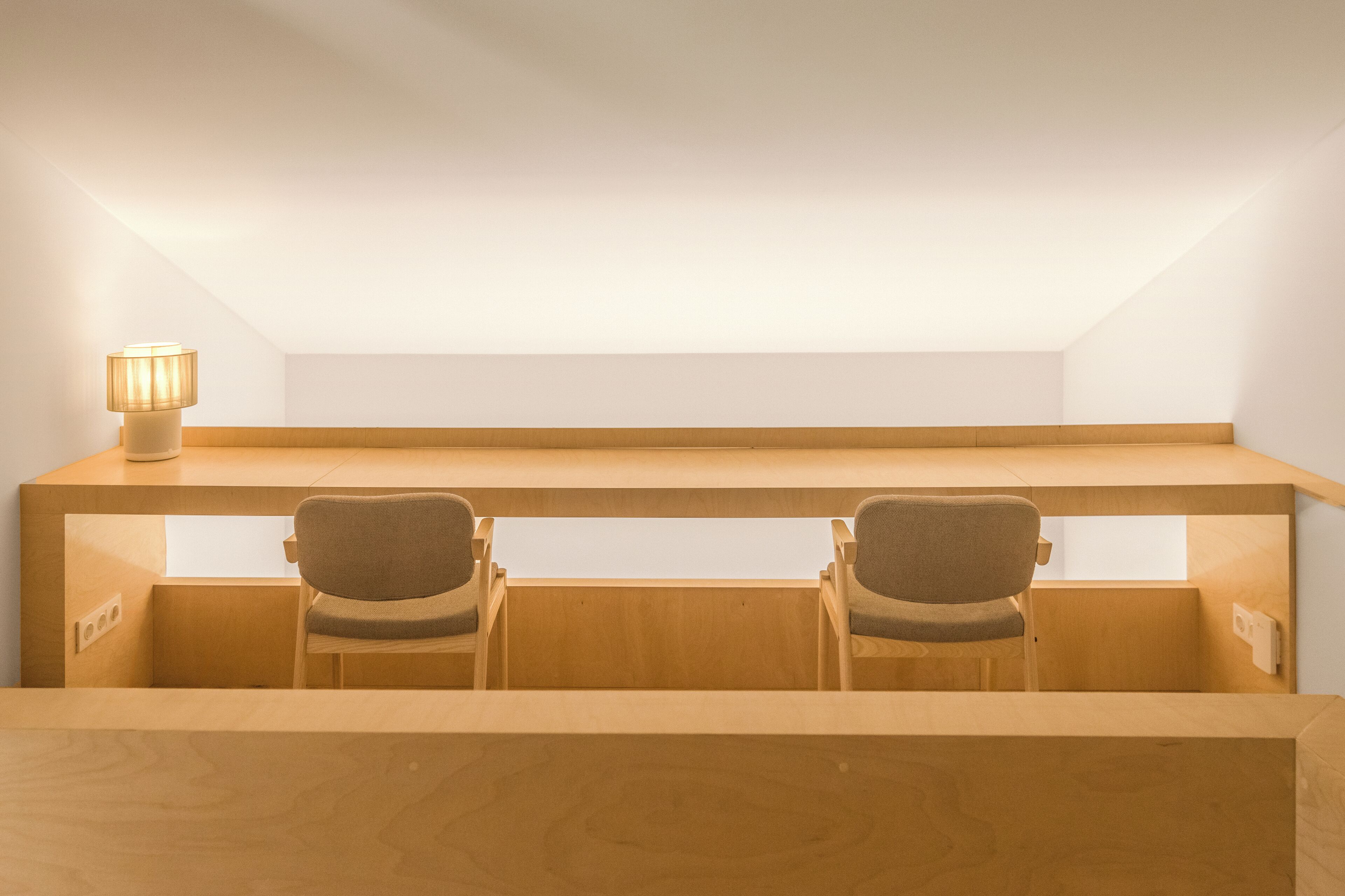 Ein kleines, helles Schlafzimmer im Dachgeschoss mit einem Holztisch und zwei Stühlen, einer Lampe und einer geneigten Decke.