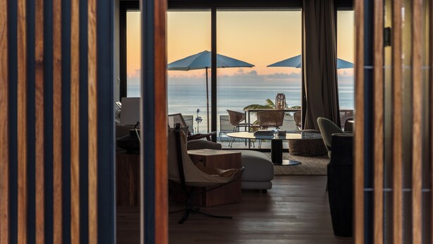 Ein modernes Wohnzimmer mit großem Fenster und Meerblick, ausgestattet mit einer Couch, Sesseln und einem kleinen Tisch.