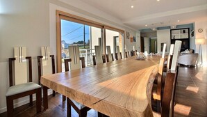 Un comedor amplio con una larga mesa de madera y sillas a juego, ventanas grandes que ofrecen vistas, y una cocina moderna al fondo.