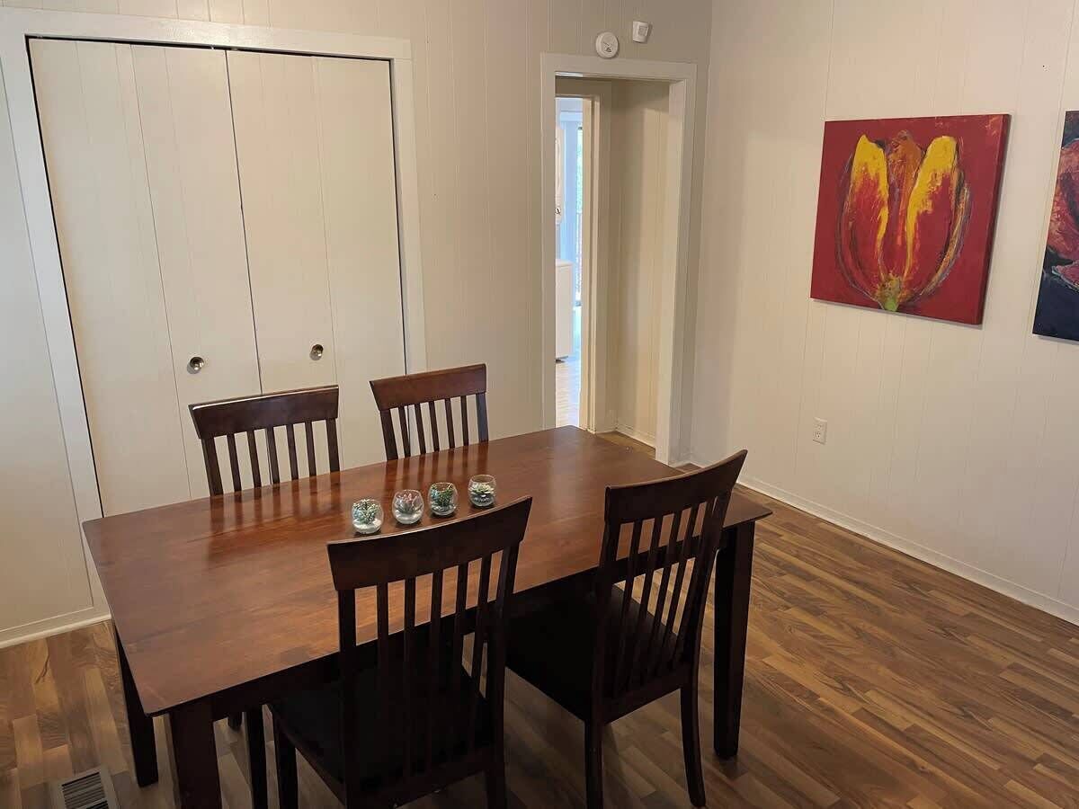 Un comedor con una mesa y sillas de madera, una puerta y un cuadro en la pared.
