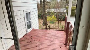 Ein Holzdeck mit Metallgeländer, eine Tür zu einem weißen Gebäude und ein kleines Fenster.