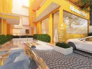 A modern hotel entrance with a yellow facade, a reception desk, and a car parked in front. - Bloom Hotel - CR Park (New Delhi)