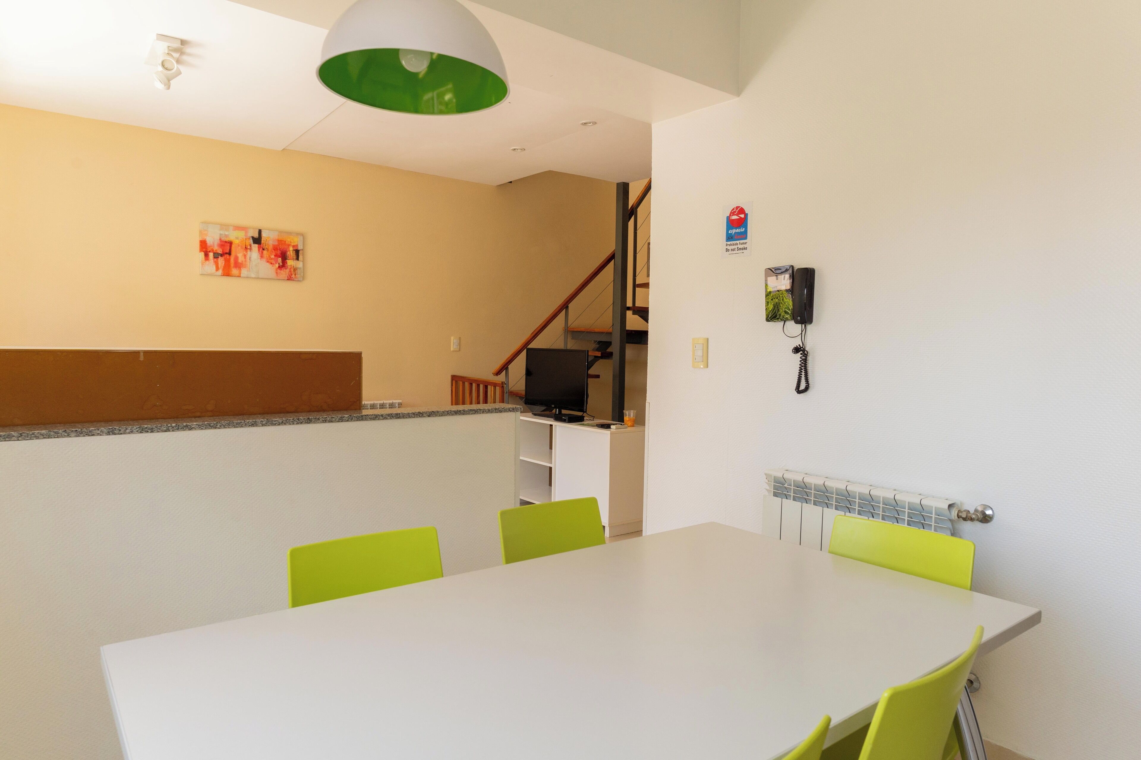 A modern dining area with a white table and green chairs, a television, and a telephone on the wall.