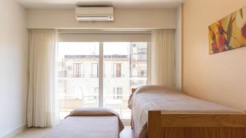 Een slaapkamer met twee bedden, een raam met gordijnen en uitzicht op gebouwen.