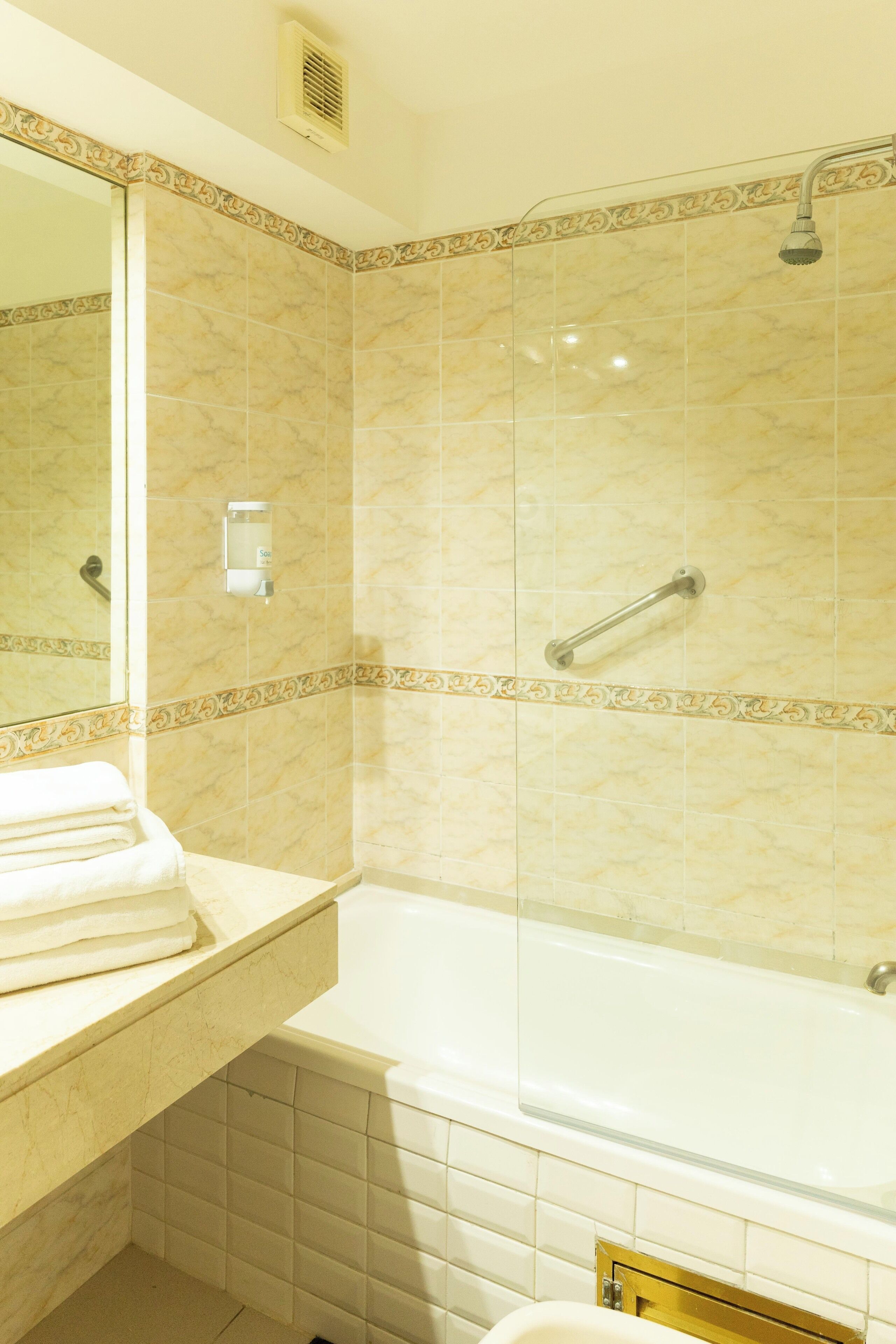 Une salle de bain avec une douche à parois de verre, une baignoire blanche et un meuble-lavabo surmonté d’une pile d’serviettes.