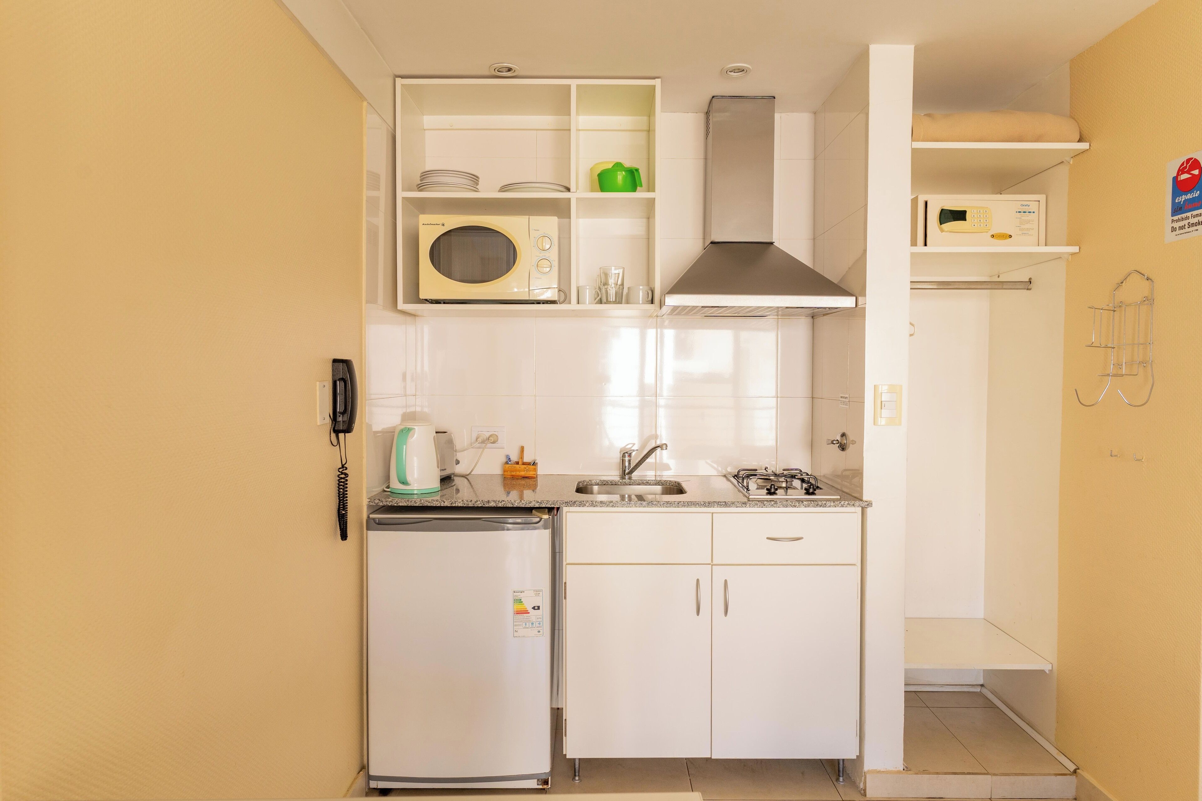 Una cucina compatta con forno a microonde integrato, un piccolo frigorifero e un lavandino.