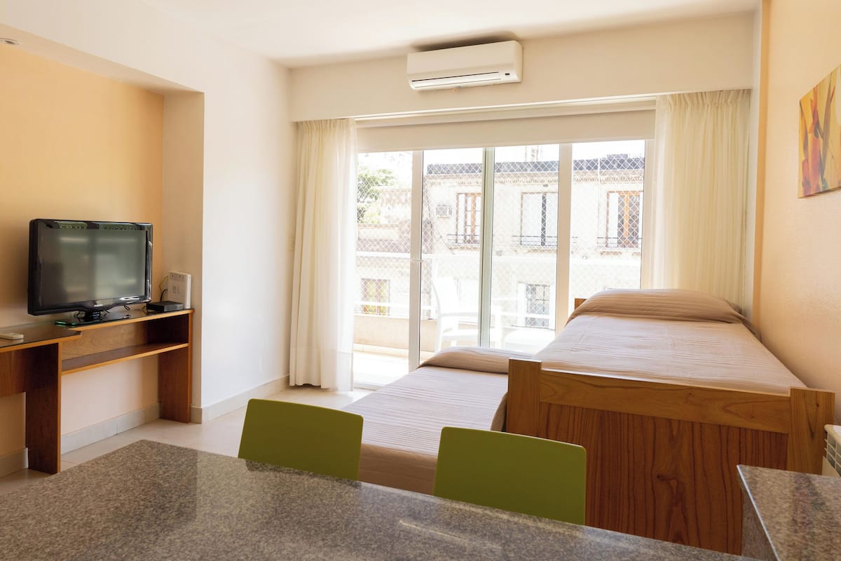 Una habitación de hotel con cama, escritorio, computadora, televisor y ventana con cortinas.