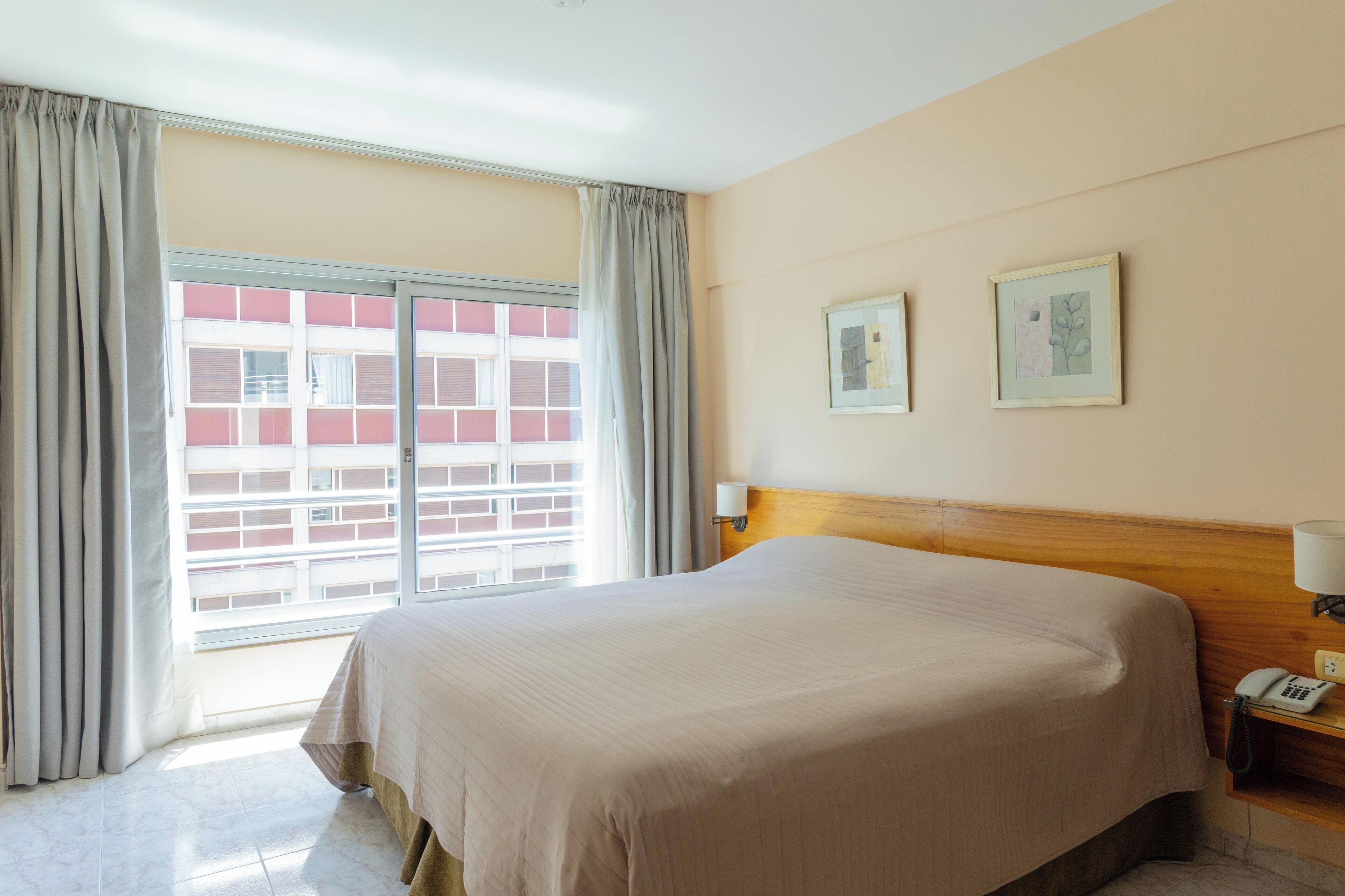 Quarto de hotel com uma cama grande, cabeceira de madeira, telefone ao lado da cama e duas molduras na parede.