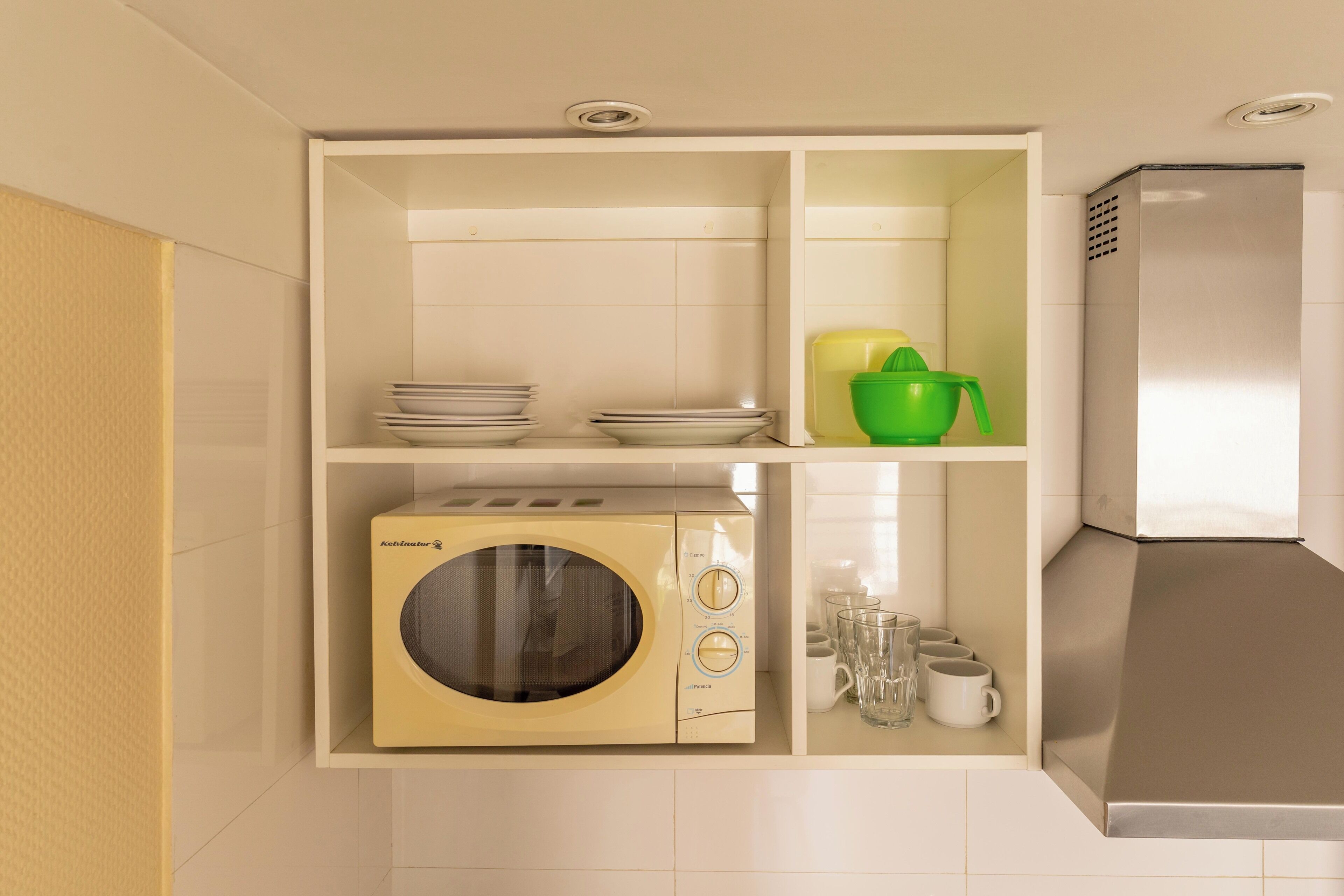 Una cocina compacta con microondas, un lavamanos pequeño y una campana extractora de acero inoxidable.