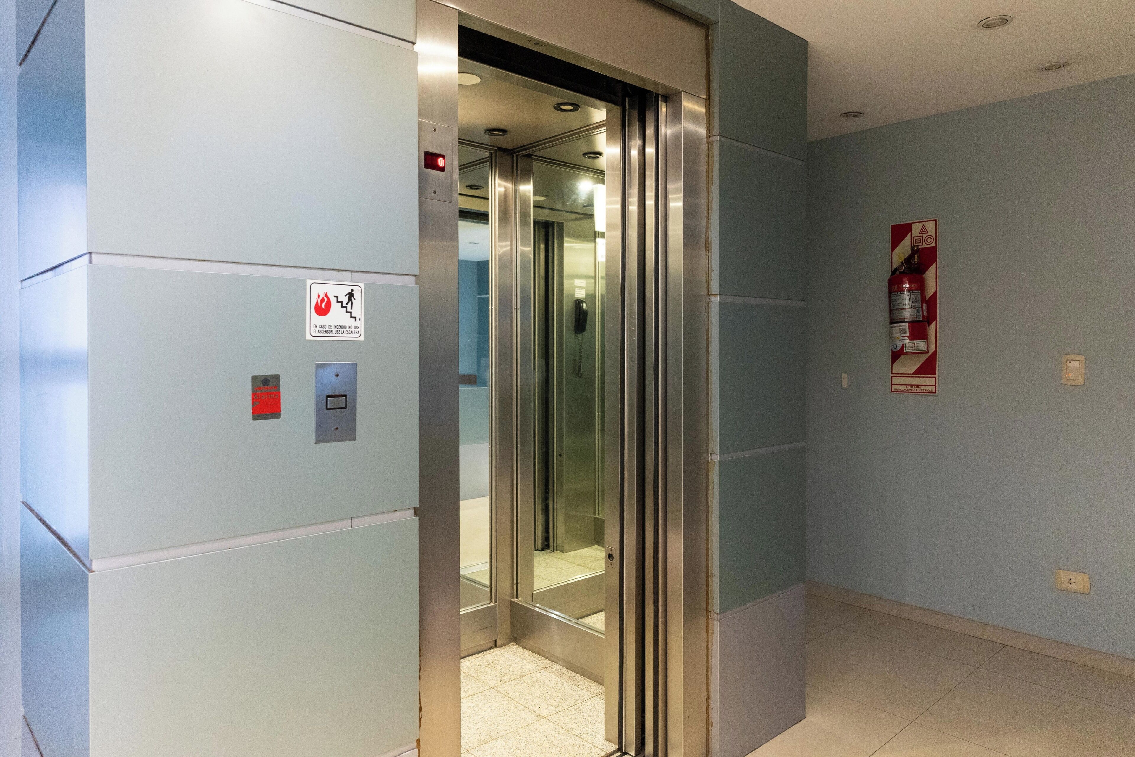 Un ascensor con un cartel de salida de incendios, un extintor y un panel de control.