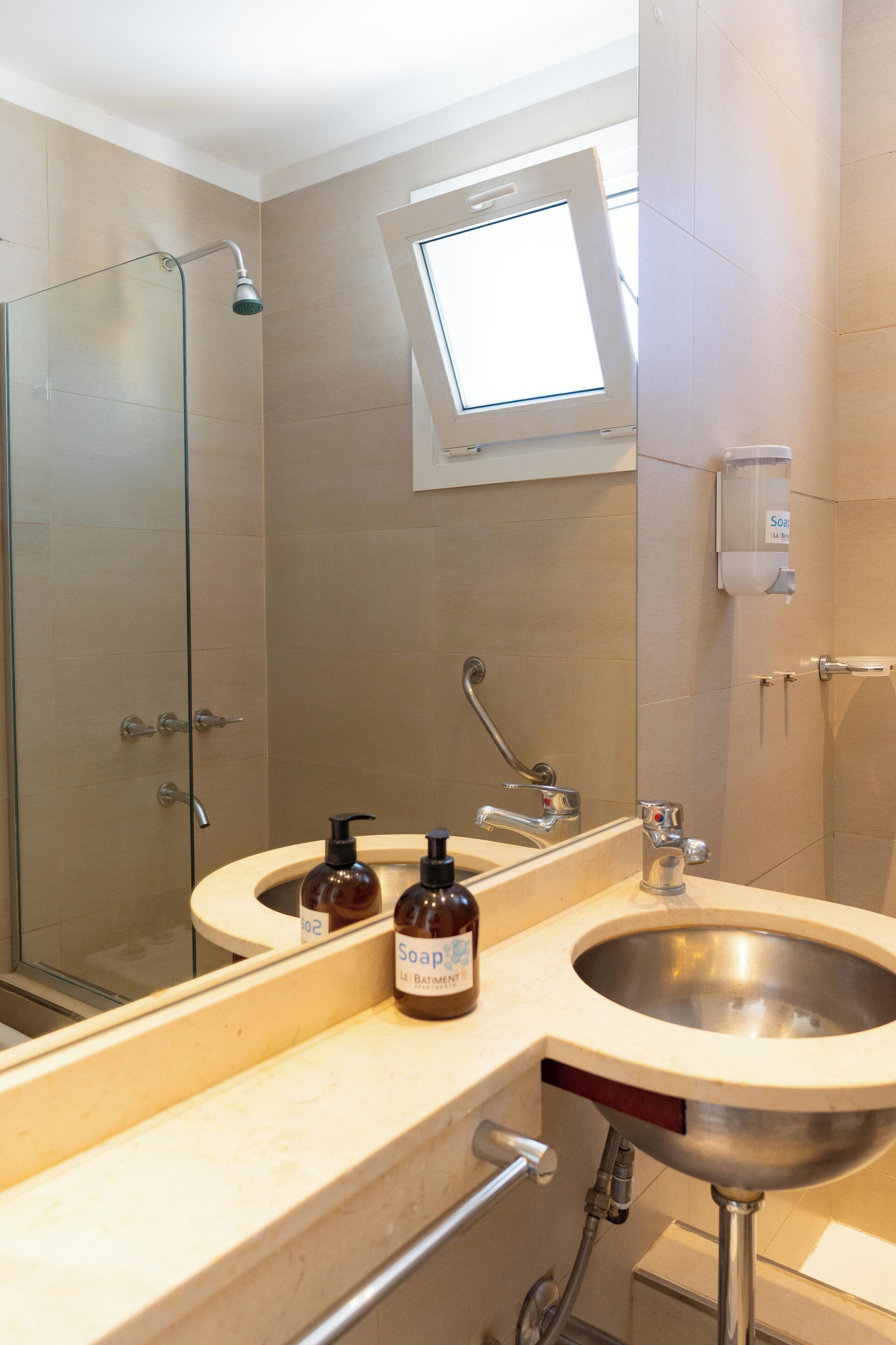 A bathroom with a glass shower enclosure, a sink with a mirror, and a window above the mirror.