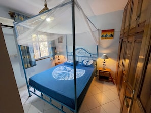 Une chambre à coucher avec un lit à baldaquin, deux tables de chevet avec des lampes, une fenêtre avec des rideaux et une porte avec un placard.