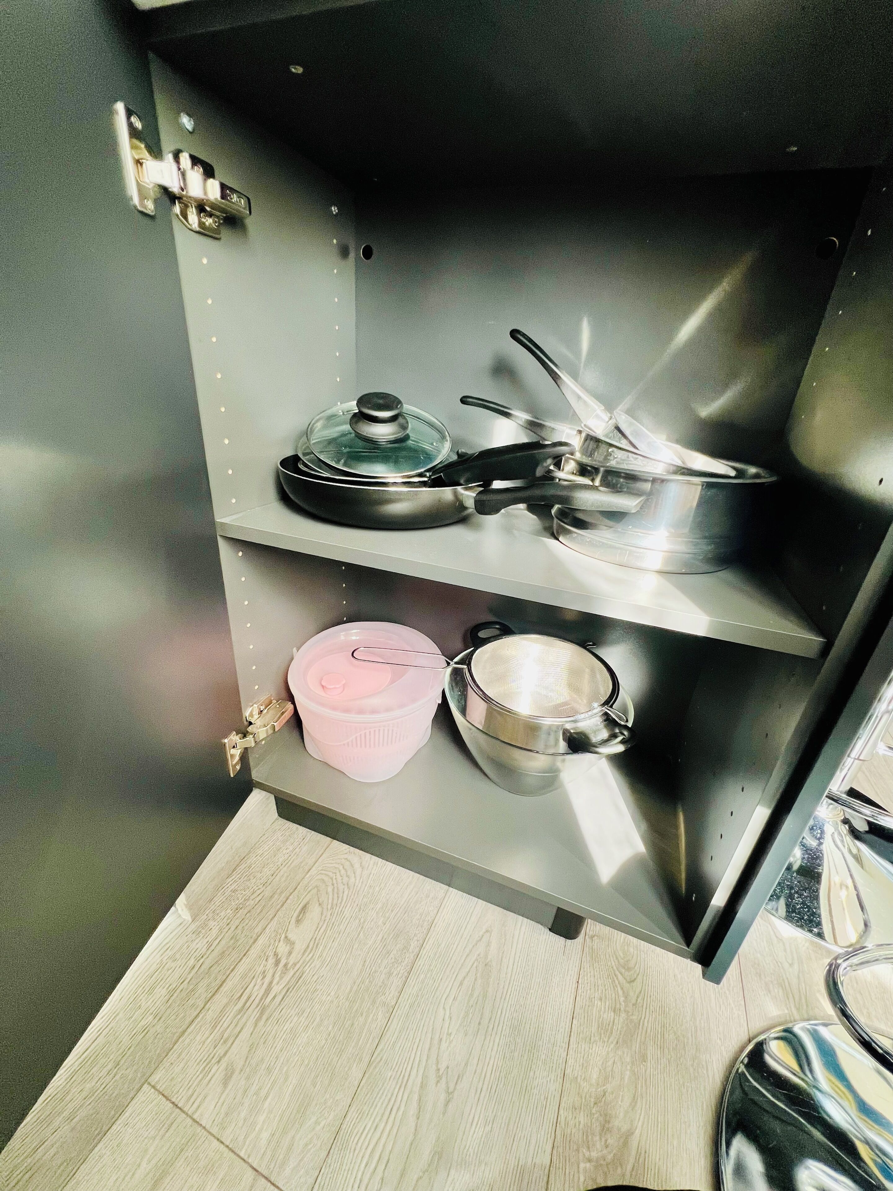 A kitchen with stainless steel appliances, a wooden floor, and a built-in shelf with cookware.