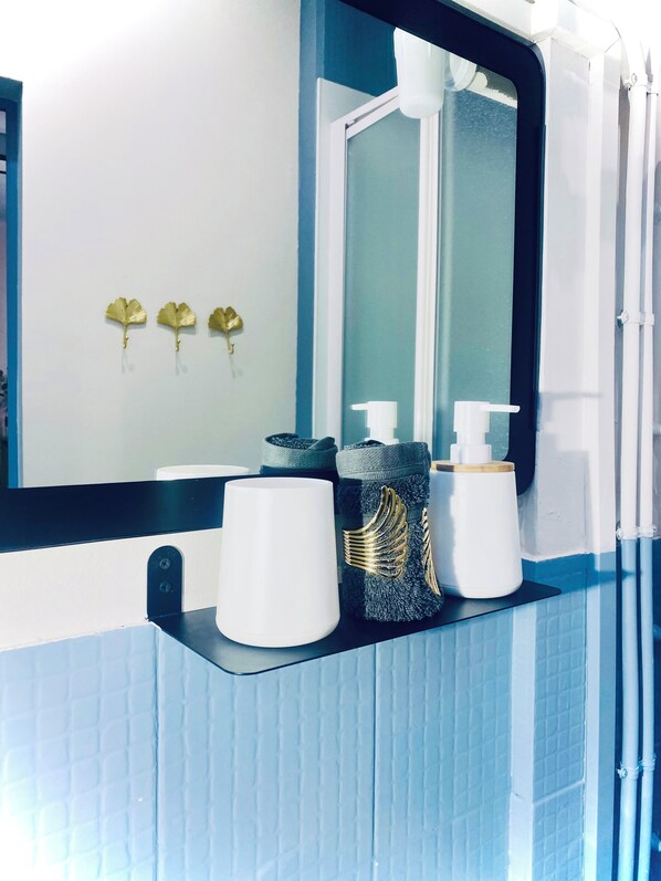 Un baño con espejo, lavamanos y tres adornos dorados con forma de hoja.
