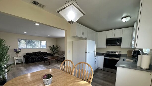 A modern kitchen with white cabinets, a built-in oven, and a dining area with a wooden table and chairs.