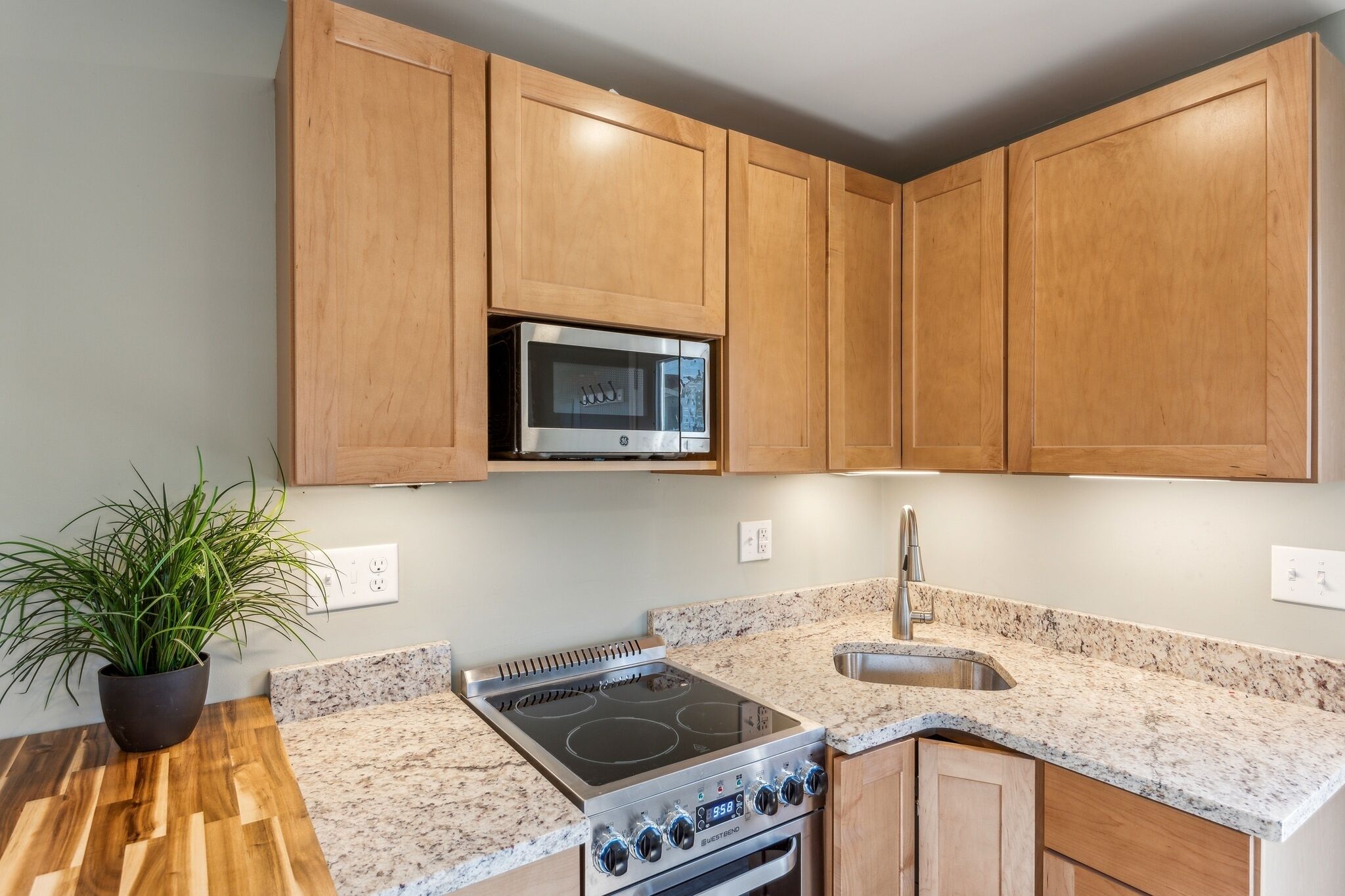 A kitchen with wooden cabinets, a stainless steel stove, a microwave, and a granite countertop.