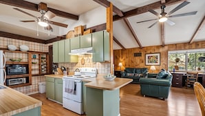 Une cuisine spacieuse avec un plancher en bois, des armoires vertes et un îlot central. On y trouve également un coin repas avec un canapé vert et une table en bois.