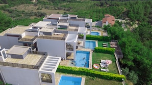 A modern residential complex with multiple buildings, rooftop terraces, and a central swimming pool surrounded by greenery. - Exclusive Villas (Kusadasi)
