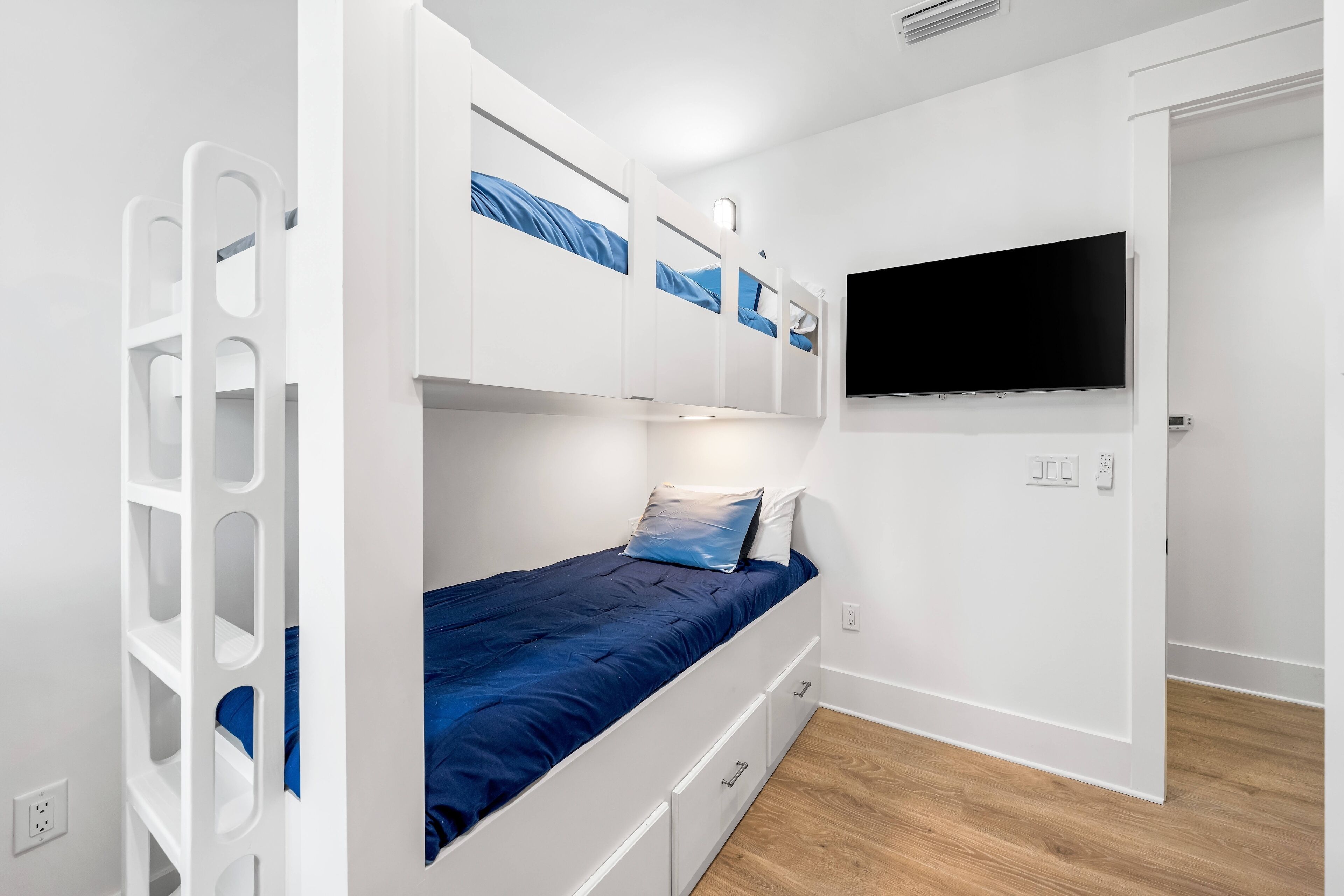 A bunk bed with a TV mounted above it, a white wardrobe, and a wooden floor.