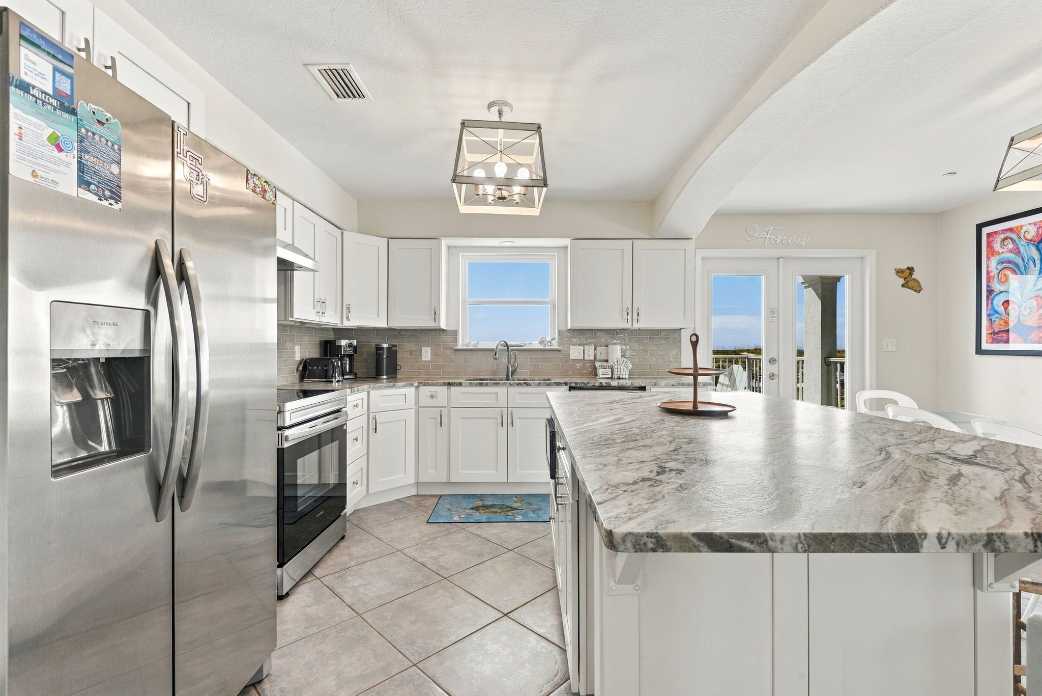 A modern kitchen with stainless steel appliances, white cabinetry, and a marble countertop.