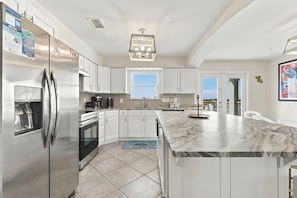 A modern kitchen with stainless steel appliances, white cabinetry, and a marble countertop.