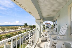 Ein Balkon mit weißen Stühlen mit Blick auf einen Strand und eine Straße.