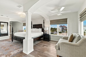 Une chambre spacieuse avec un grand lit, une table de chevet, une chaise et une vue sur une maison par la fenêtre.