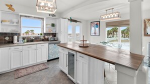 A modern kitchen with white cabinetry, a wooden countertop, and a view of palm trees.