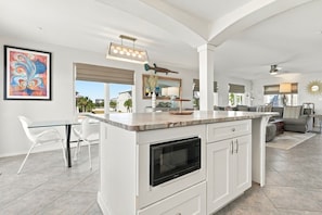 A modern kitchen with a central island, white cabinetry, and a large window offering a view of the outdoors.