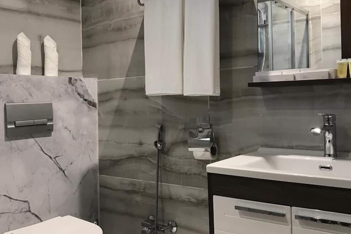 Een moderne badkamer met een marmeren wand, een wit toilet, een glazen douchecabine en een wastafel met een spiegel.