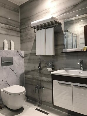 A modern bathroom with a marble wall, a white toilet, a glass shower enclosure, and a vanity with a mirror. - East Garden Plus Serviced apartments شقق حديقة الشرق بلس للشقق المخدومة  (Al Khobar)