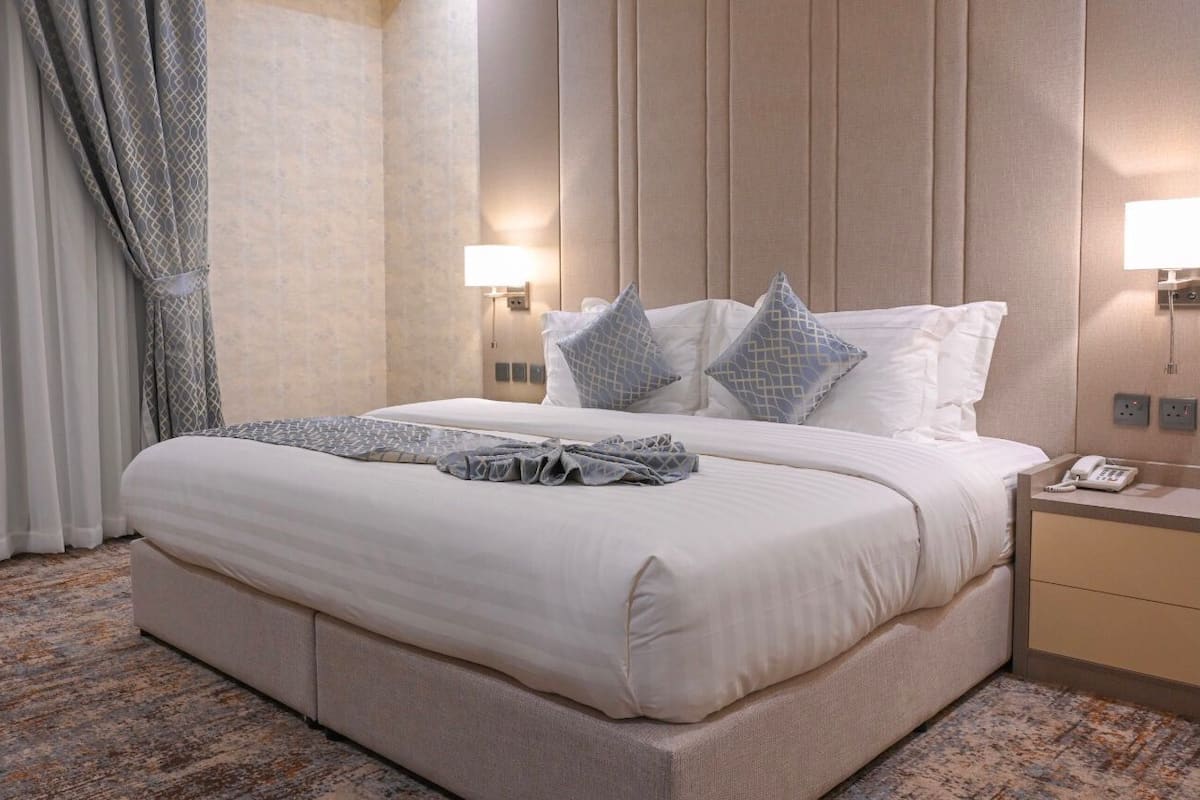 Hotelkamer met een groot bed, nachtkastje met telefoon en een wandlamp.