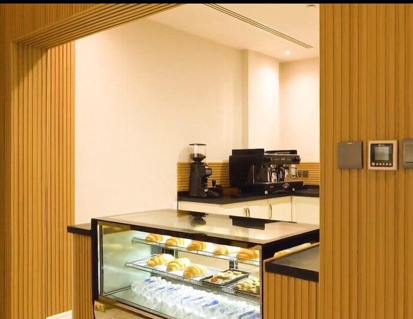 A hotel room with a breakfast bar, a coffee machine, and a glass display case with pastries.