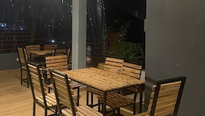 An outdoor dining area with wooden tables and chairs, a covered ceiling, and a view of the night sky. - Zeyman's Apartments (Kigali)