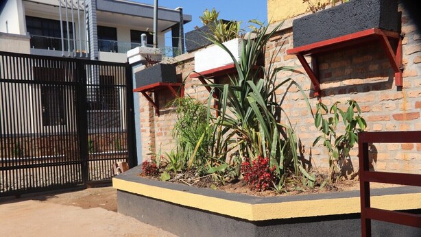 A residential area with a gated entrance, a brick wall, and a planter box with plants. - Zeyman's Apartments (Kigali)