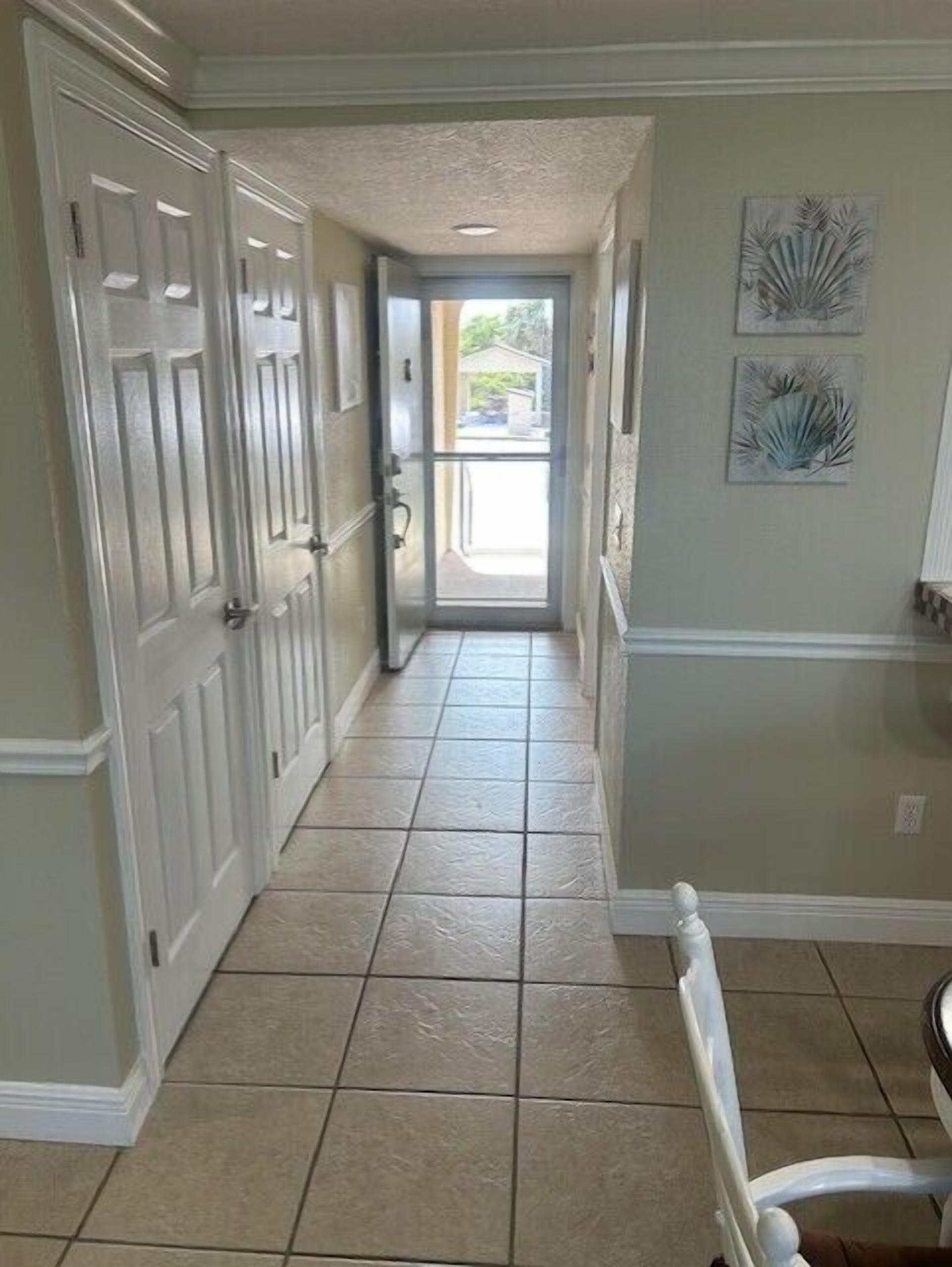A hallway with white doors, a tiled floor, and two wall-mounted artworks.