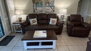 A living room with a brown leather sofa set, a white coffee table, and a ceiling fan. - Direct Oceanview Premium Flat with 2 Bed/2 Bath +Murphy Bed. Just Renovated! (St. Augustine)