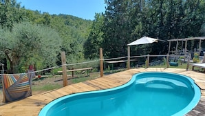 A wooden deck with a swimming pool, surrounded by a fence and trees. - Villa de Luccheri - Stay in Nature (Frasso Telesino)