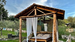 A rustic wooden gazebo with a bed, surrounded by a stone wall and greenery. - Villa de Luccheri - Stay in Nature (Frasso Telesino)