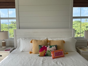 A bed with white bedding, two pillows with tassels, and a colorful pillow with a quote.