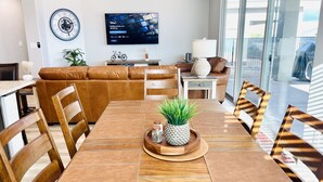 Ein modernes Wohnzimmer mit einem braunen Ledersofa, einem Holzesstisch und Stühlen. Ein Flachbildfernseher an der Wand zeigt einen Disney Sender.