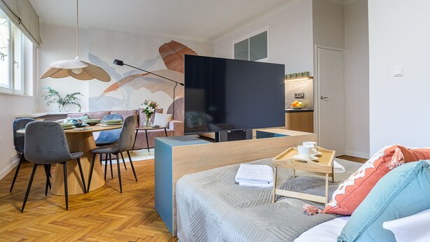 A modern hotel room with a dining area, a large flat-screen TV, a bed with a wooden headboard, and a small kitchenette. - Apartament Wiejska I (Warsaw)