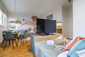 A modern hotel room with a dining area, a large flat-screen TV, a bed with a wooden headboard, and a small kitchenette. - Apartament Wiejska I (Warsaw)