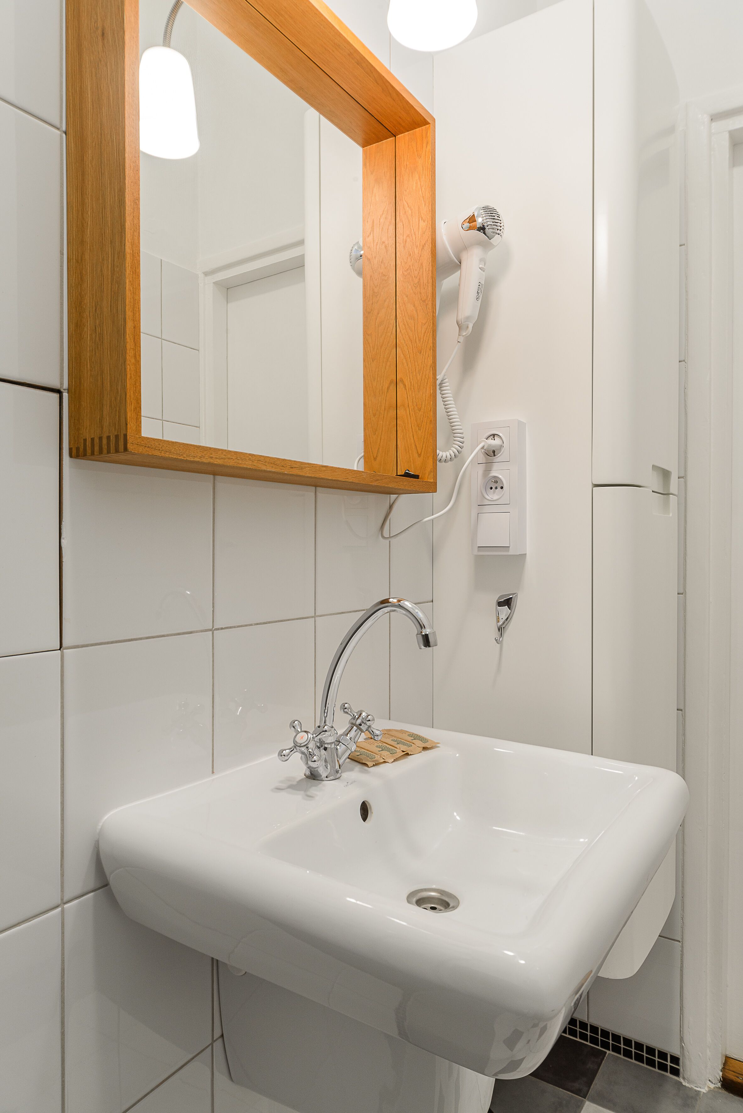 Ein Badezimmer mit einem weißen Waschbecken, einem spiegel mit Holzrahmen und einem an der Wand befestigten Föhn.