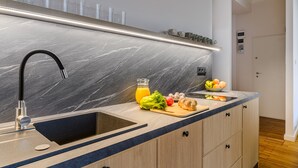 A modern kitchen with a black sink, marble backsplash, and wooden cabinets. - Apartament Wiejska I (Warsaw)