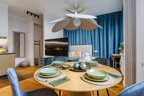 Ein moderner Essraum mit einem Holztisch, gedeckt für vier Personen, einem Deckenventilator und einem angrenzenden Küchenbereich.