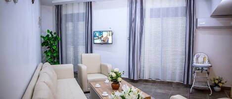 A modern living room with a sofa set, a coffee table with flowers, and a TV on the wall.