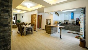 Eine moderne Küche mit Kochinsel, ein Essbereich mit Tisch und Stühlen sowie ein Wohnzimmer mit Sofa und Fernseher.