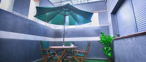 A small, enclosed patio area with a table and chairs, a green umbrella, and a potted plant.